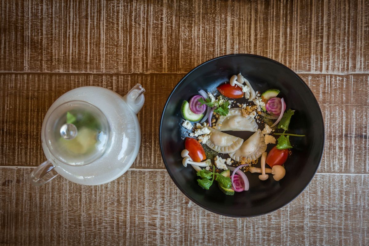 A black plate with a salad and a clear glass mug on a wooden table.