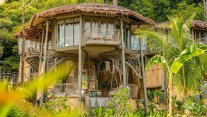 A two-story house with a thatched roof, multiple balconies, and a lush garden. - TreeHouse Villas - TreeHouse Villa (Ko Yao Noi)