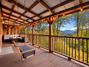 Une terrasse en bois avec un fauteuil suspendu, un canapé et un foyer.