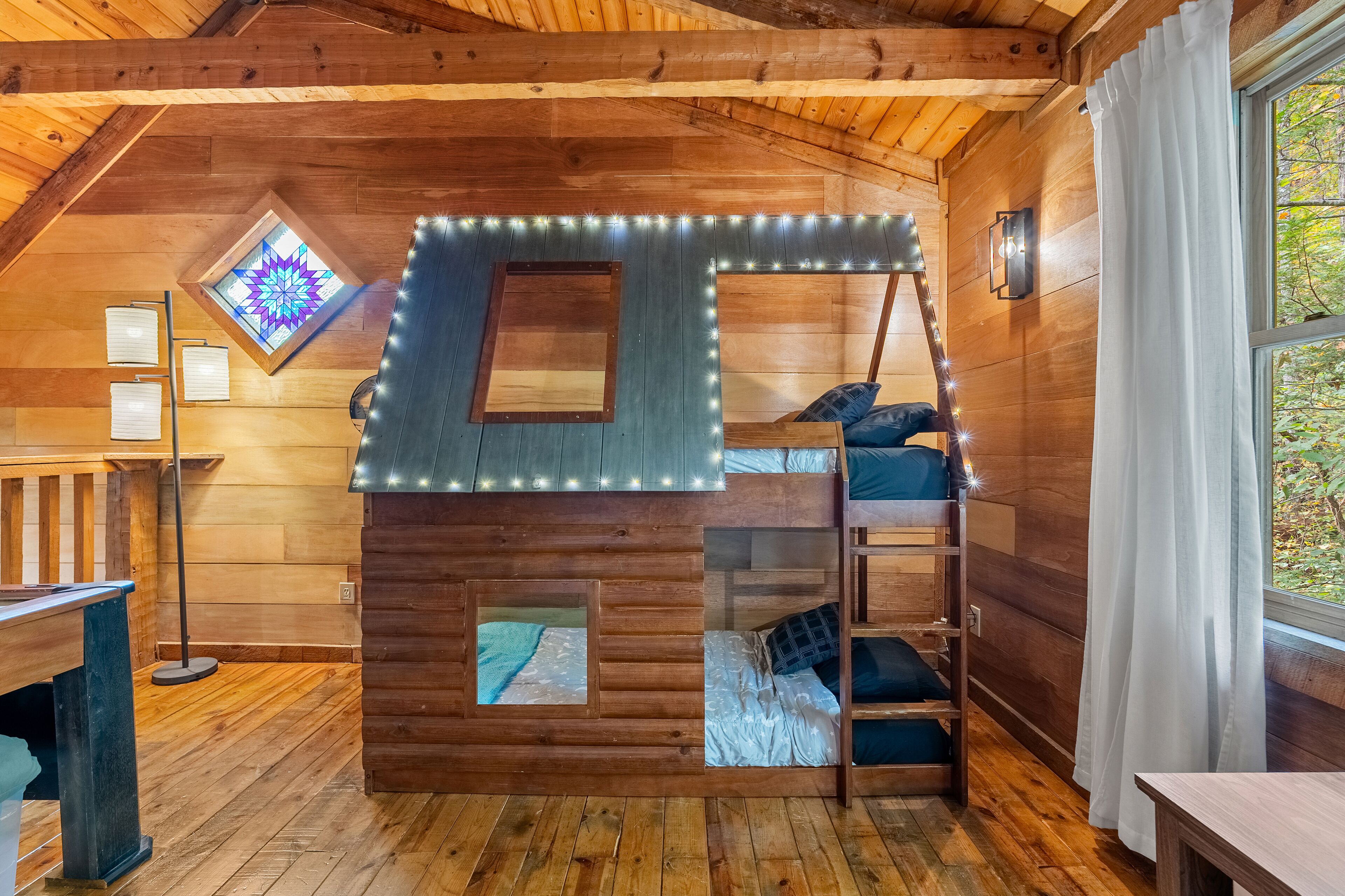 Una cabaña acogedora con una cama en el altiloque, un ventanal con diseño de estrellas y una escalera al camarote superior.