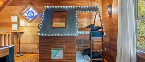 Una cabaña acogedora con una cama en el altiloque, un ventanal con diseño de estrellas y una escalera al camarote superior.