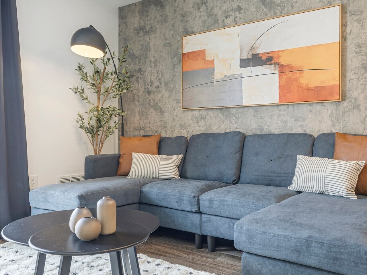 Un salon moderne avec un canapé d’angle gris, une table basse ronde et un lampadaire.