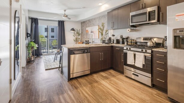 Una cocina moderna con electrodomésticos de acero inoxidable, armarios de madera oscura y piso de madera.