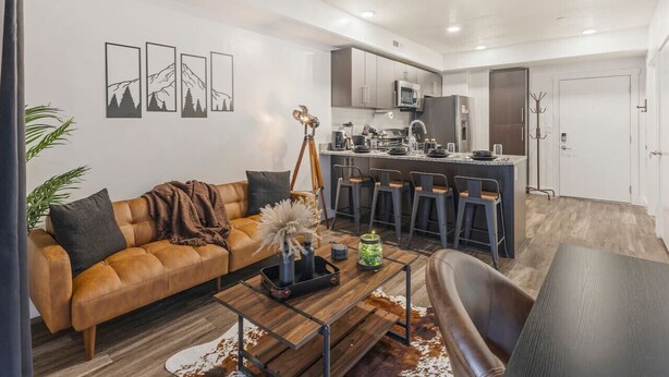 A modern living room with a sofa, coffee table, and a dining area with bar stools.