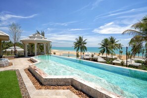 Ein Pool mit klarem, blauem Wasser, umgeben von Palmen und Blick auf den Strand.