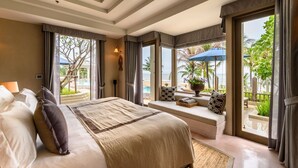 A spacious bedroom with a large bed, a seating area with a view of the beach, and a balcony with umbrellas.