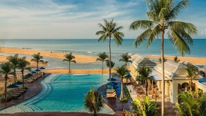 A resort with a swimming pool, beach, and palm trees.