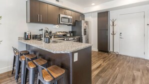 A modern kitchen with dark wood cabinets, stainless steel appliances, a granite countertop, and a bar area with stools.