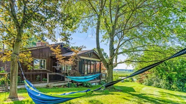 A wooden house with a porch, two hammocks, and a grassy yard.