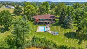 A large house with a swimming pool, surrounded by a well-maintained lawn and trees.