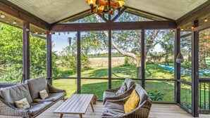 A covered patio with wicker furniture and a table, overlooking a garden.
