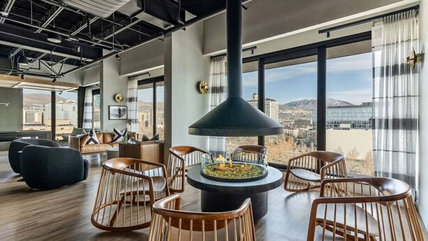 A modern lounge area with a central fire feature, comfortable seating, and large windows offering a city view.