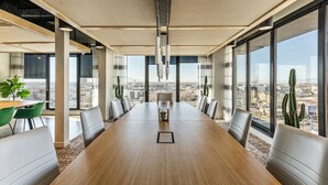 A conference room with a long table, chairs, and large windows offering a city view.
