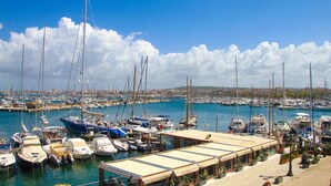 A marina with numerous boats docked, a covered area with seating, and a view of the town in the background. - Amazing apartment in Alghero with house sea view (Alghero)