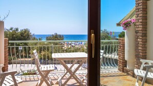 A balcony with a view of the beach, white outdoor furniture, and a brick wall with flowers. - Amazing apartment in Alghero with house sea view (Alghero)