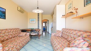 A living room with two patterned sofas, a dining table with chairs, and a kitchen area in the background. - Amazing apartment in Alghero with house sea view (Alghero)