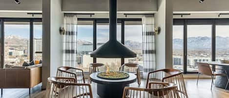 Relax in a spacious room with a central seating area, round table, and six chairs, offering a view of the surrounding mountains and city.