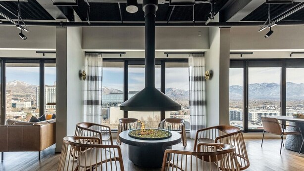 A modern interior with a central fire feature, large windows, and a view of a cityscape. - DT Studio | Gym | Pool Table | 12th Floor |Parking (Salt Lake City)