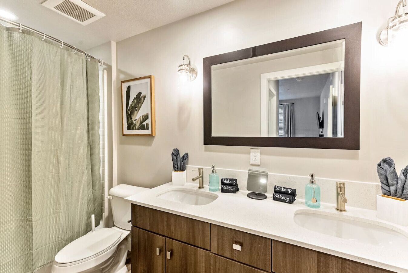 A bathroom with a white sink, two mirrors, a framed picture, and a shower curtain.