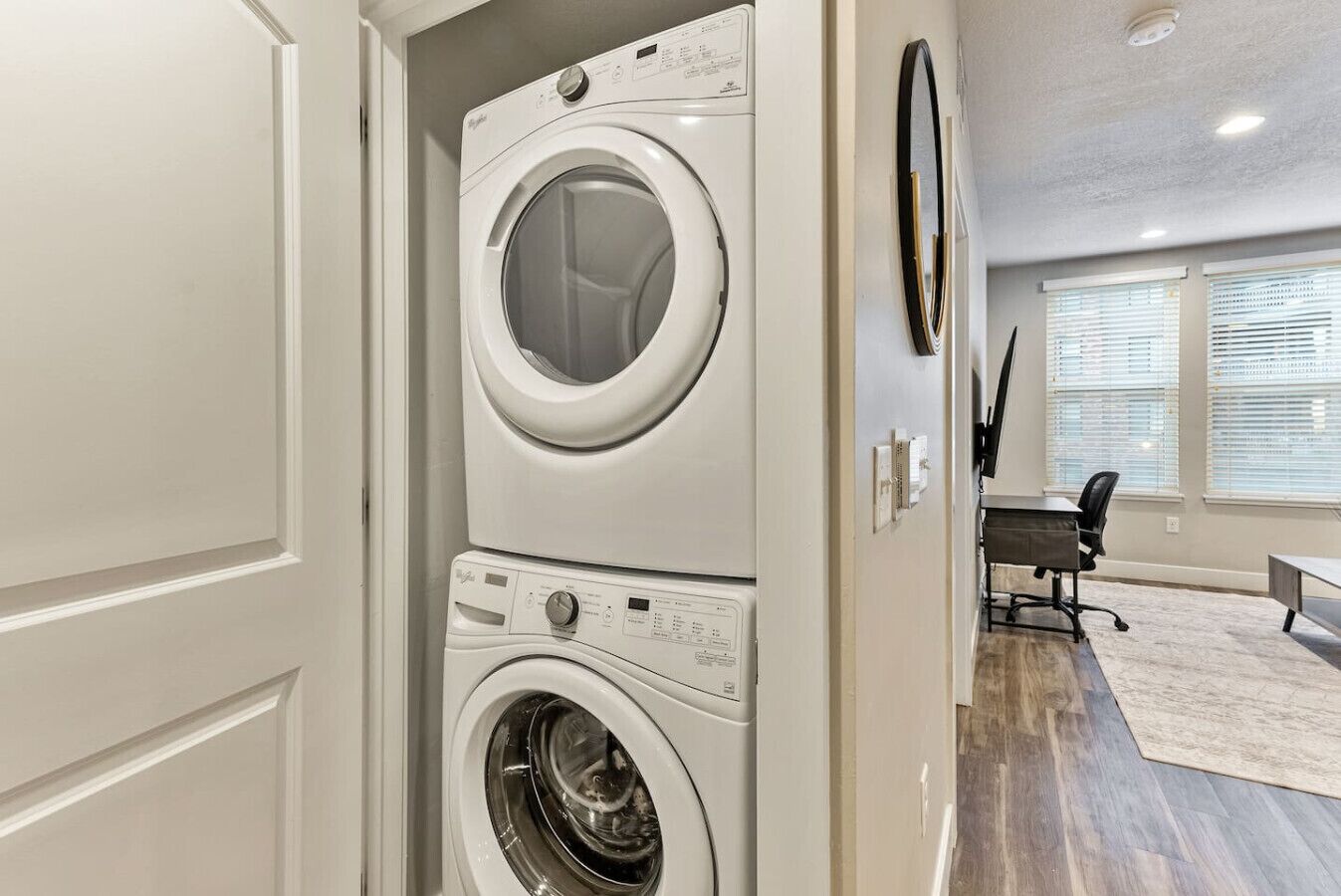 A laundry room with a stacked washer and dryer, a desk, and a chair.