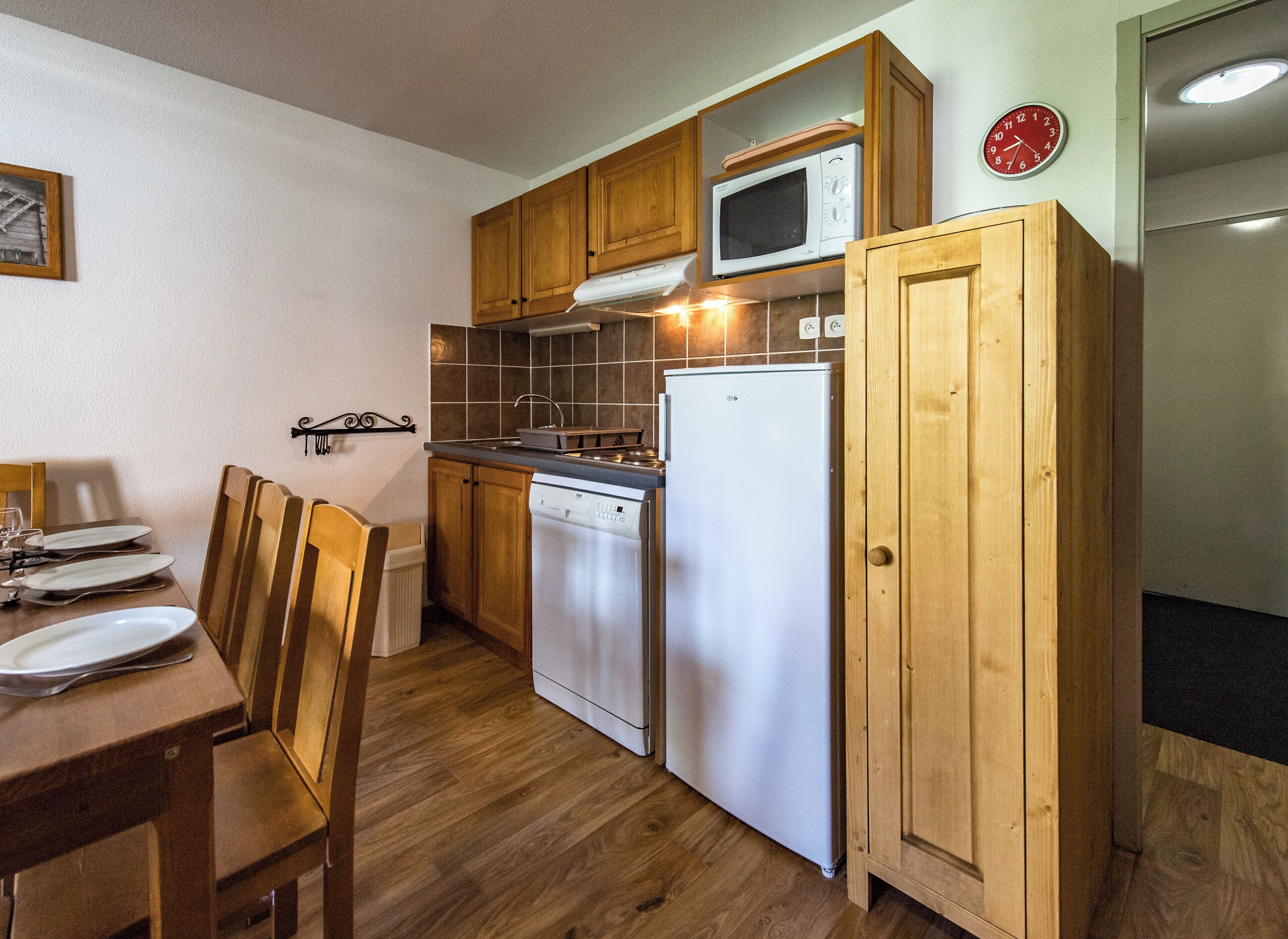 Una cocina compacta con armarios de madera, un microondas, un lavavajillas y un refrigerador.