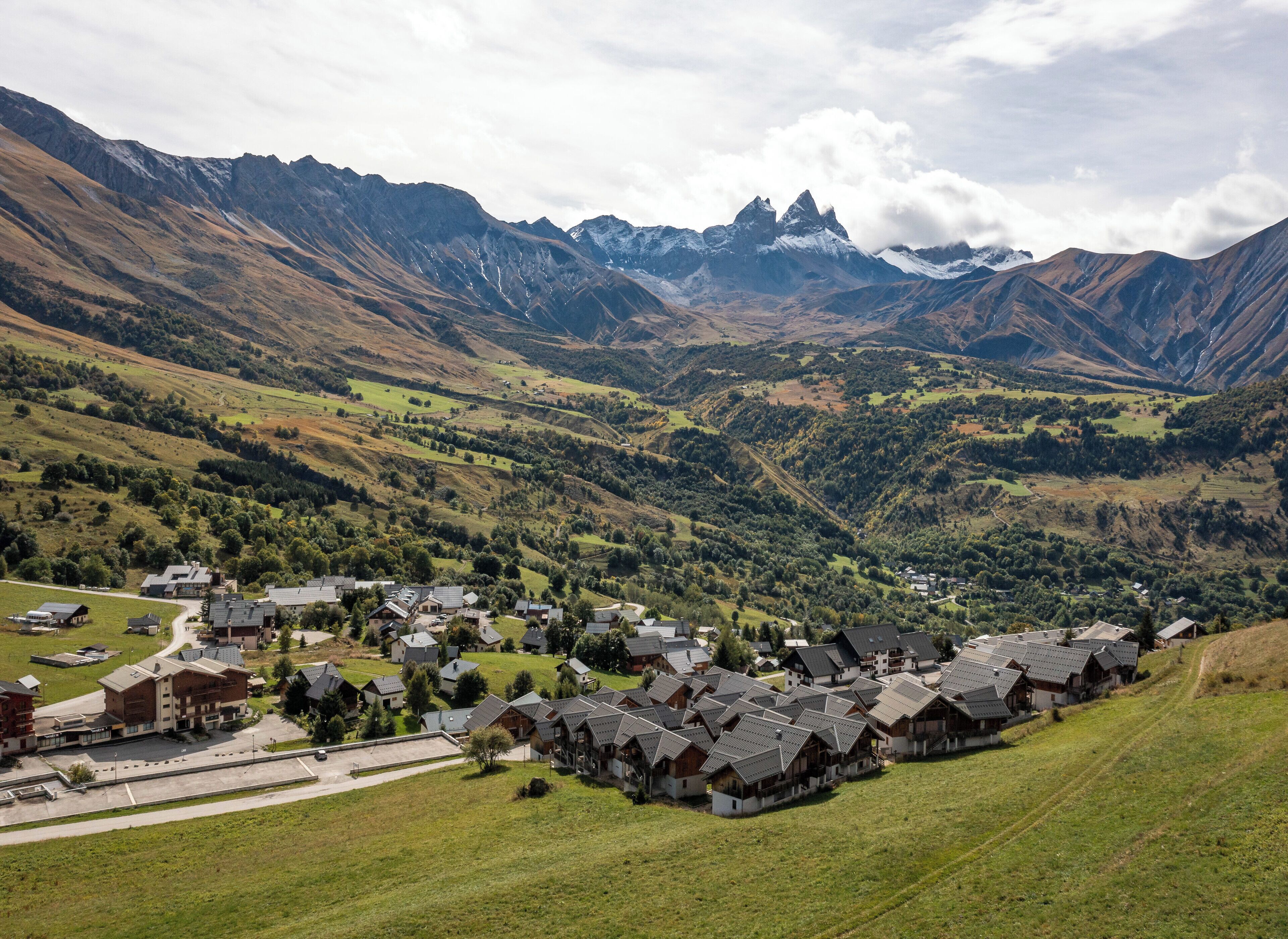 Un pueblo montañoso con casas tradicionales, una calle principal y vistas a picos distantes.