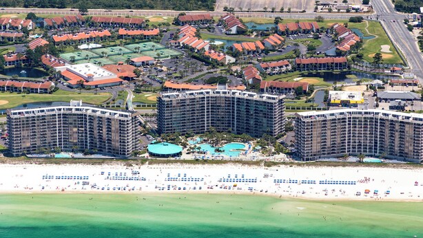 A coastal resort with multiple high-rise buildings, a central pool area, and a beach with umbrellas. - 2BR Golf Retreat, Sleeps 8 Comfortably (Panama City Beach)
