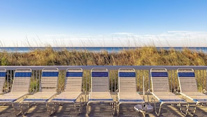 A row of beachside lounge chairs with a view of the ocean and tall grasses in the background. - 2BR Golf Retreat, Sleeps 8 Comfortably (Panama City Beach)