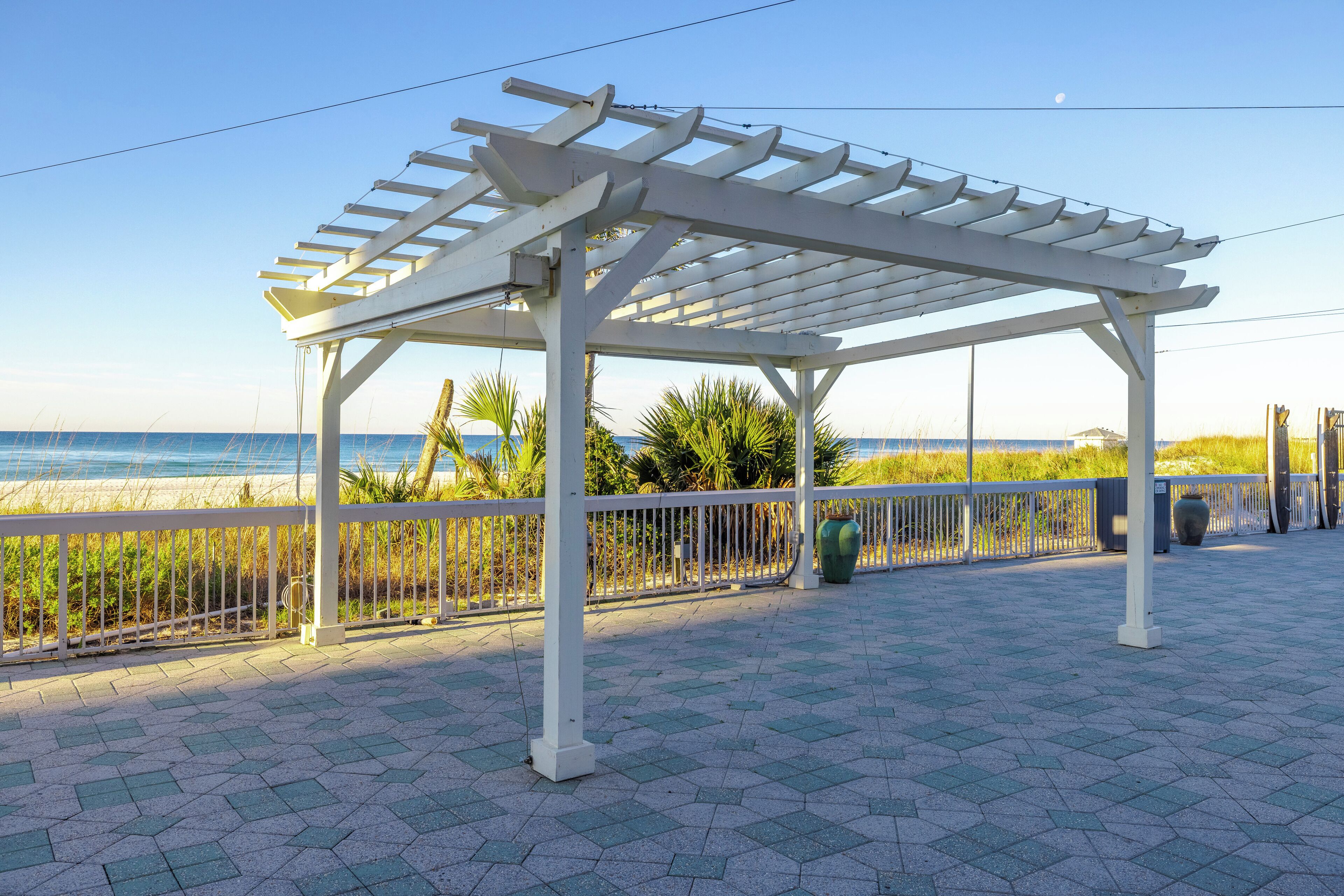 A covered outdoor area with a white pergola, a tiled floor, and a view of the beach.