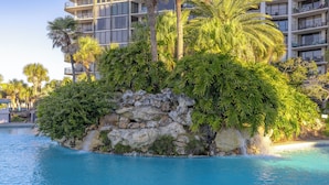 A pool surrounded by lush greenery and a rocky island. - 2BR Golf Retreat, Sleeps 8 Comfortably (Panama City Beach)