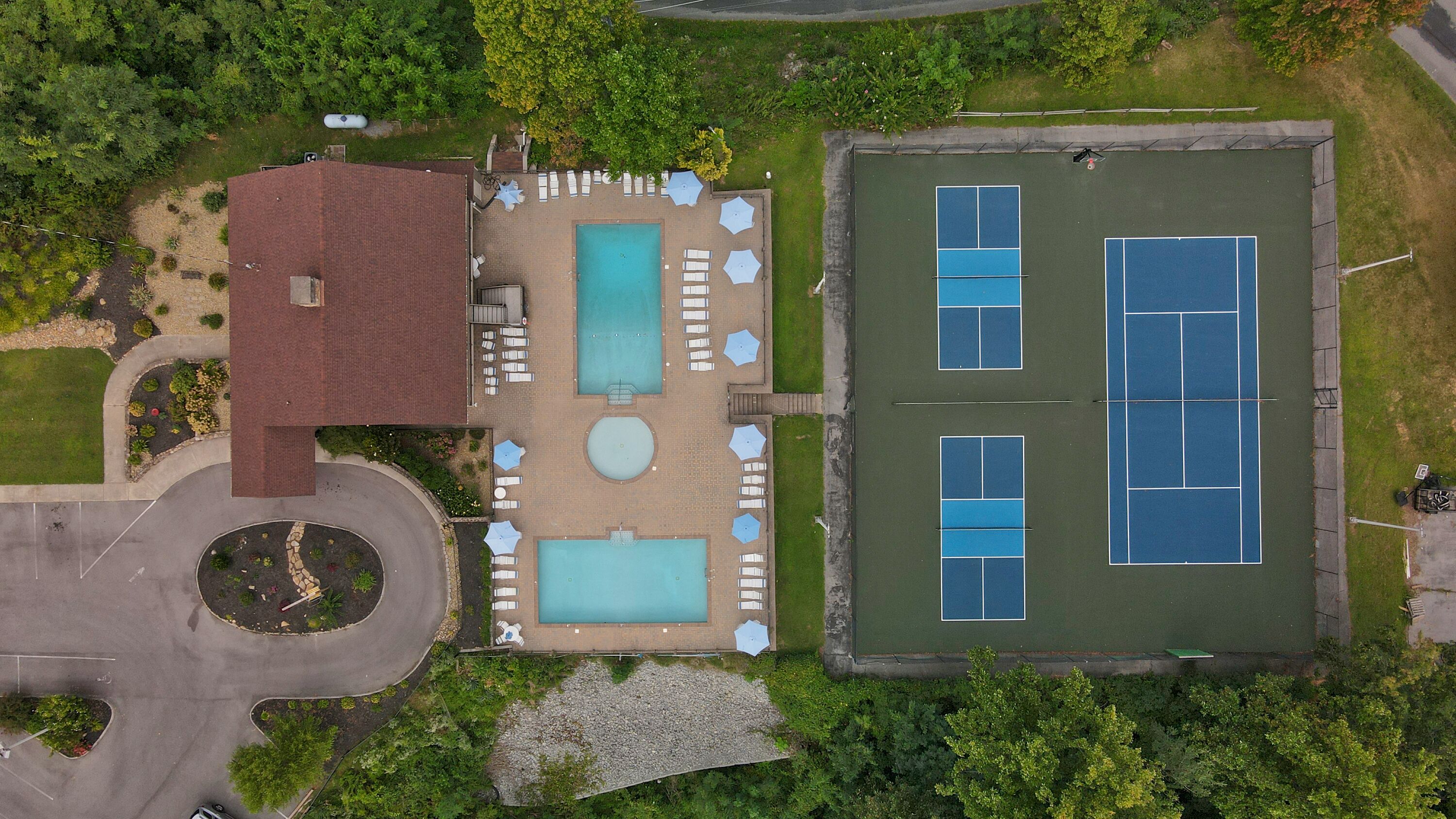 Eine Vogelperspektive eines Anwesens mit Schwimmbad, Liegestühlen, Tennisplatz und überdachter Terrasse.