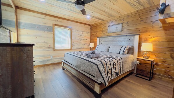 Un dormitorio con paneles de madera, una cama, lámparas de noche y un ventilador de techo.