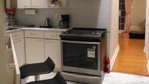 A modern kitchen with white cabinets, a stainless steel oven, and a black bar stool. - Resort style  entire guesthouse with kitchen (2 rooms) (Loretto)