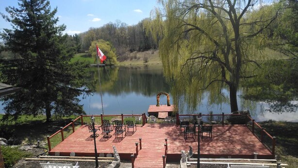 A wooden deck with chairs and tables overlooking a lake, a flag, and a gazebo. - Resort style  entire guesthouse with kitchen (2 rooms) (Loretto)