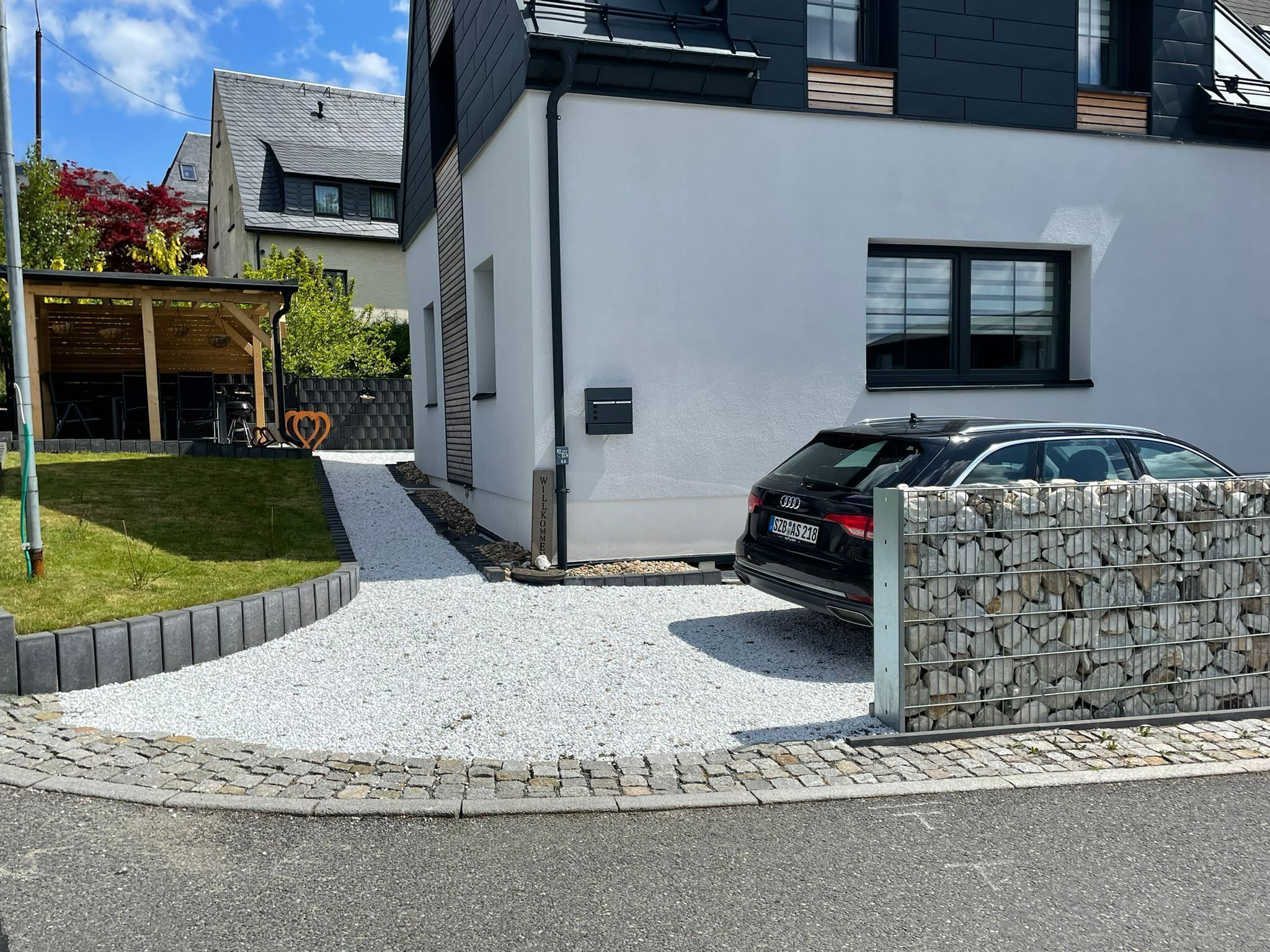 A modern two-story house with a black car parked in the driveway.