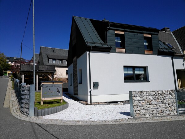 A modern two-story house with a sloped roof, a small front porch, and a stone wall. - Ferienhaus Anton Günther (Lauter-Bernsbach)
