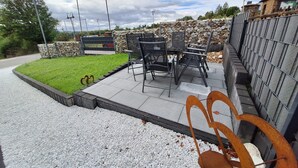 Een terras met stoelen en een tafel, omgeven door een stenen muur en een gazon.