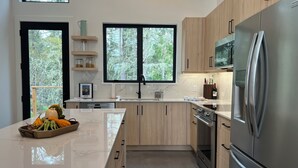 A modern kitchen with wooden cabinets, a stainless steel refrigerator, and a marble countertop. - Cliffside Hideaway: Luxurious, Peaceful, with Gorgeous views Over the Ocean (Port Renfrew)