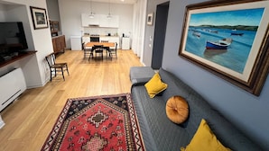A modern living room with a sofa, a rug, and a painting of boats on water. - Pisu Apartments (appart.Orsolina)  (Quartucciu)