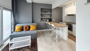 A modern apartment with a grey sofa, a dining table, and a kitchen area. - Pisu Apartments (appart.Luigino)  (Quartucciu)