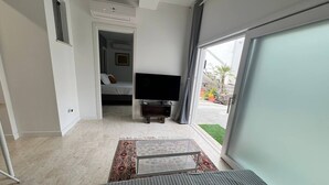 A modern living room with a sofa, a TV, and a view of the outdoors through a large window. - Pisu Apartments (appart.Luigino)  (Quartucciu)