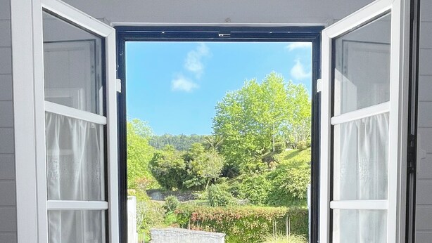 An open window with a view of a garden and a stone wall.