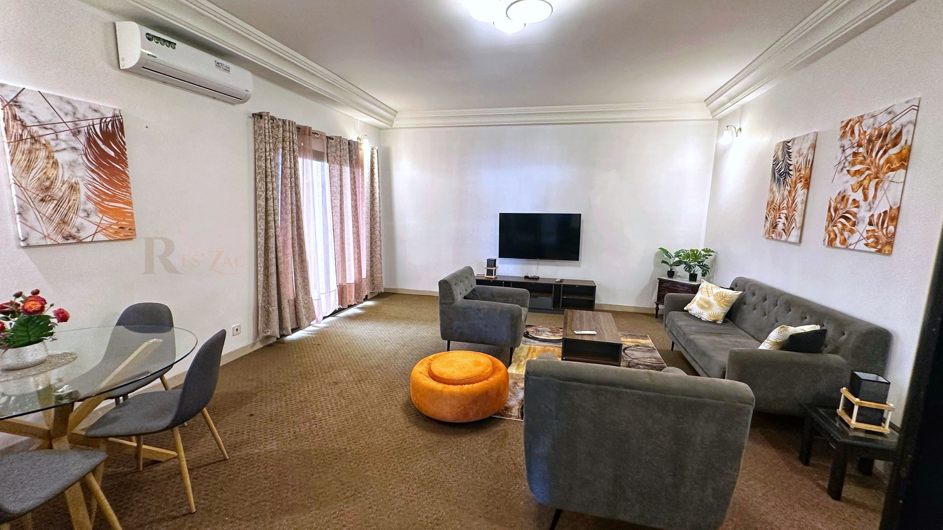 Una sala de estar moderna con un televisor de pantalla plana, sofás grises, una mesa de comedor de vidrio con sillas y decoración en la pared.