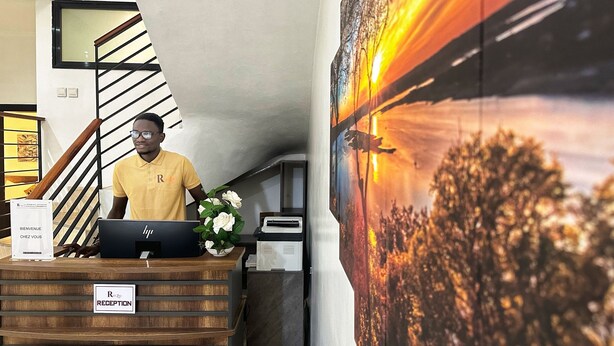 Een receptiebalie met een bordje met de tekst 'RECEPTION' en een computer. Er is een trap met een zwarte balustrade en een aan de muur bevestigd schilderij.