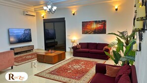 Een woonkamer met een televisie, bank, salontafel en decoratieve vloerkleden.