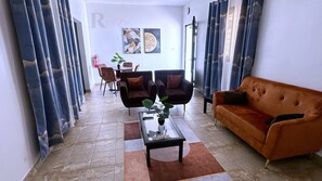 A modern living room with a sofa, two armchairs, a coffee table, and a dining area in the background. - Res'Zac (Rufisque)