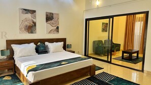 Een hotelkamer met een houten bed, twee nachtkastjes, een groene fauteuil, een tafeltje en een glazen schuifdeur die leidt naar een balkon met uitzicht.