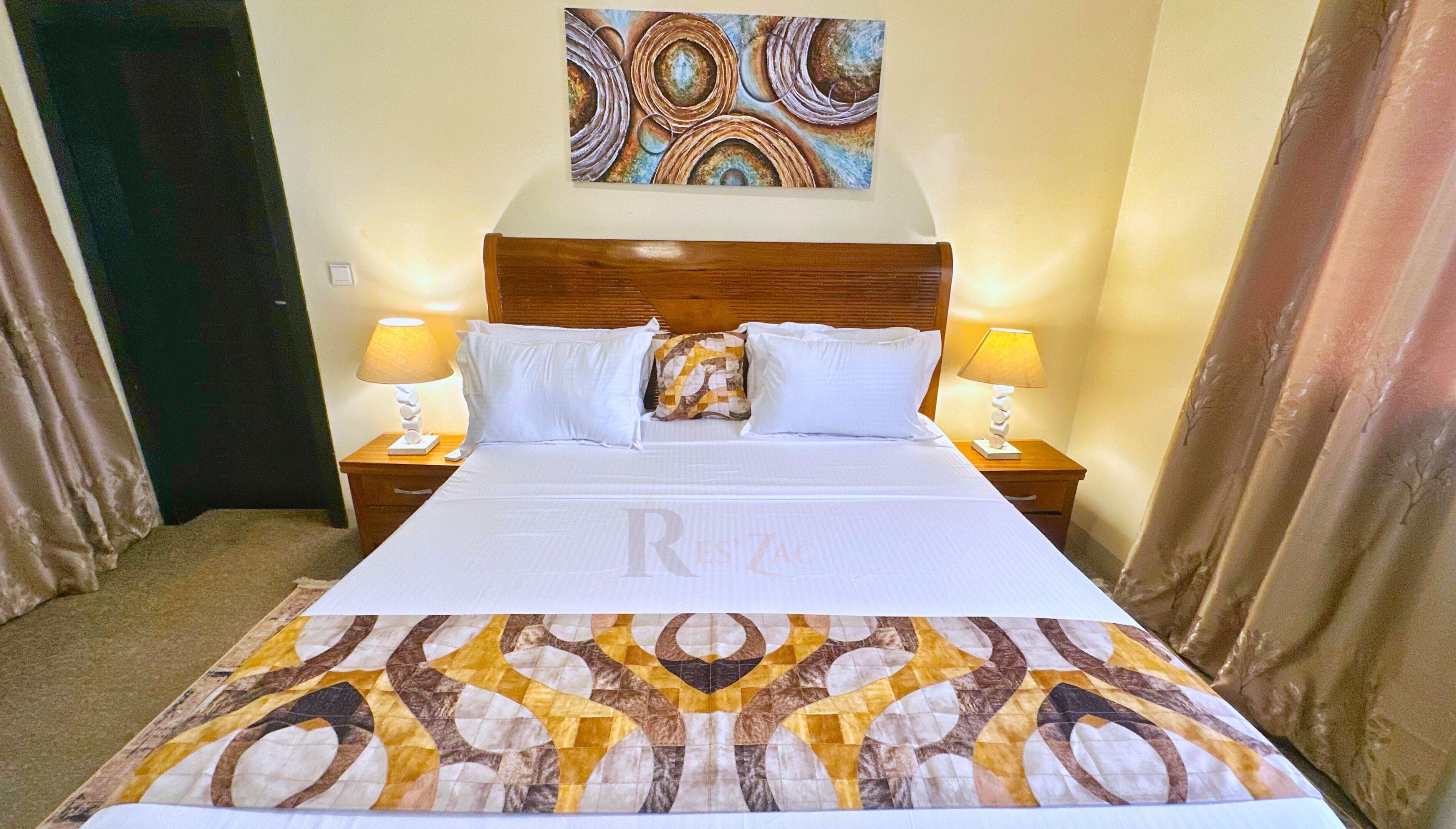 A hotel room with a large bed, two bedside tables with lamps, a headboard, and a wall painting.