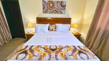A hotel room with a large bed, two bedside tables with lamps, a headboard, and a wall painting.