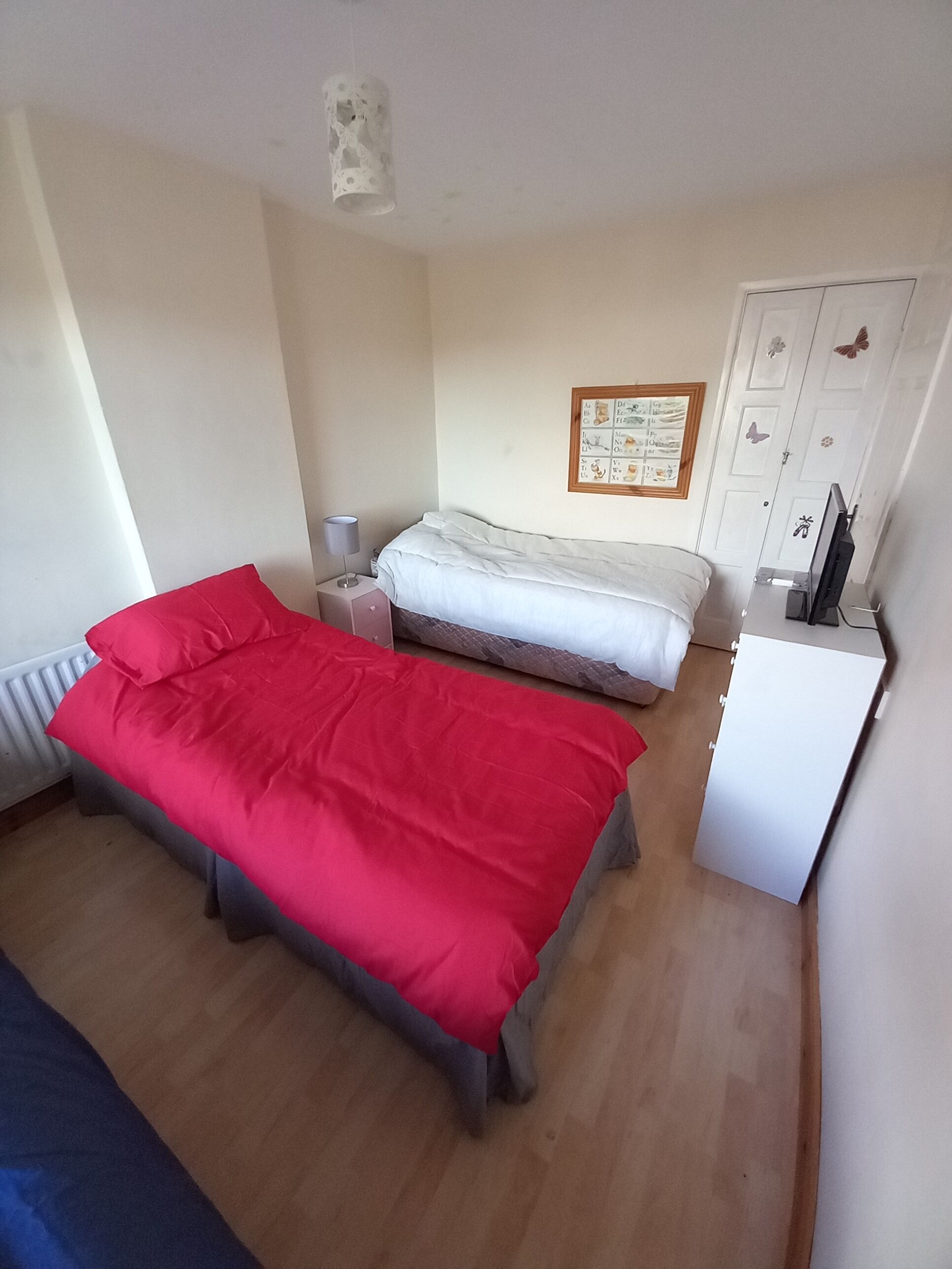 Et værelse med to senge, et skrivebord, en radiator og en væg med et billede i ramme.